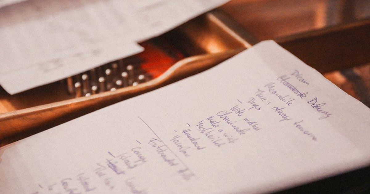 Handwritten lists on sheets of paper resting on an open grand piano, with the strings and hammers visible