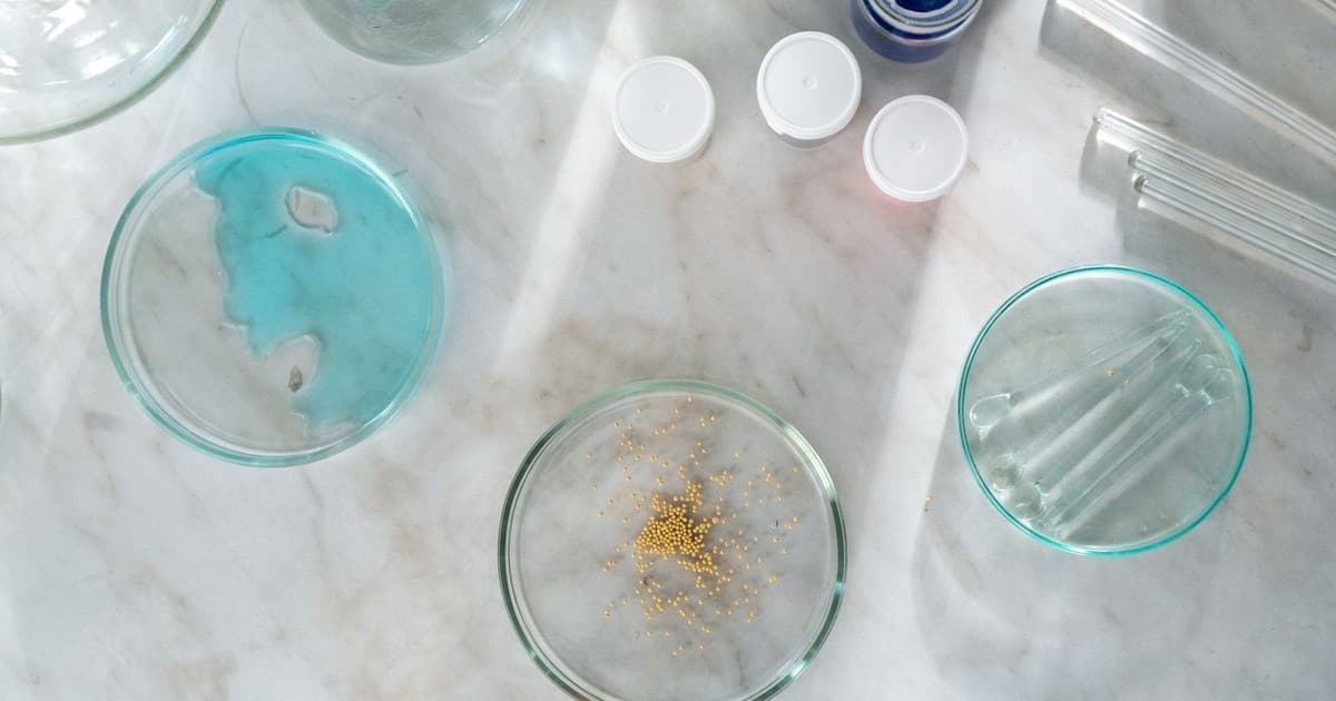 Laboratory equipment and petri dishes on a marble surface with blue liquid and golden particles