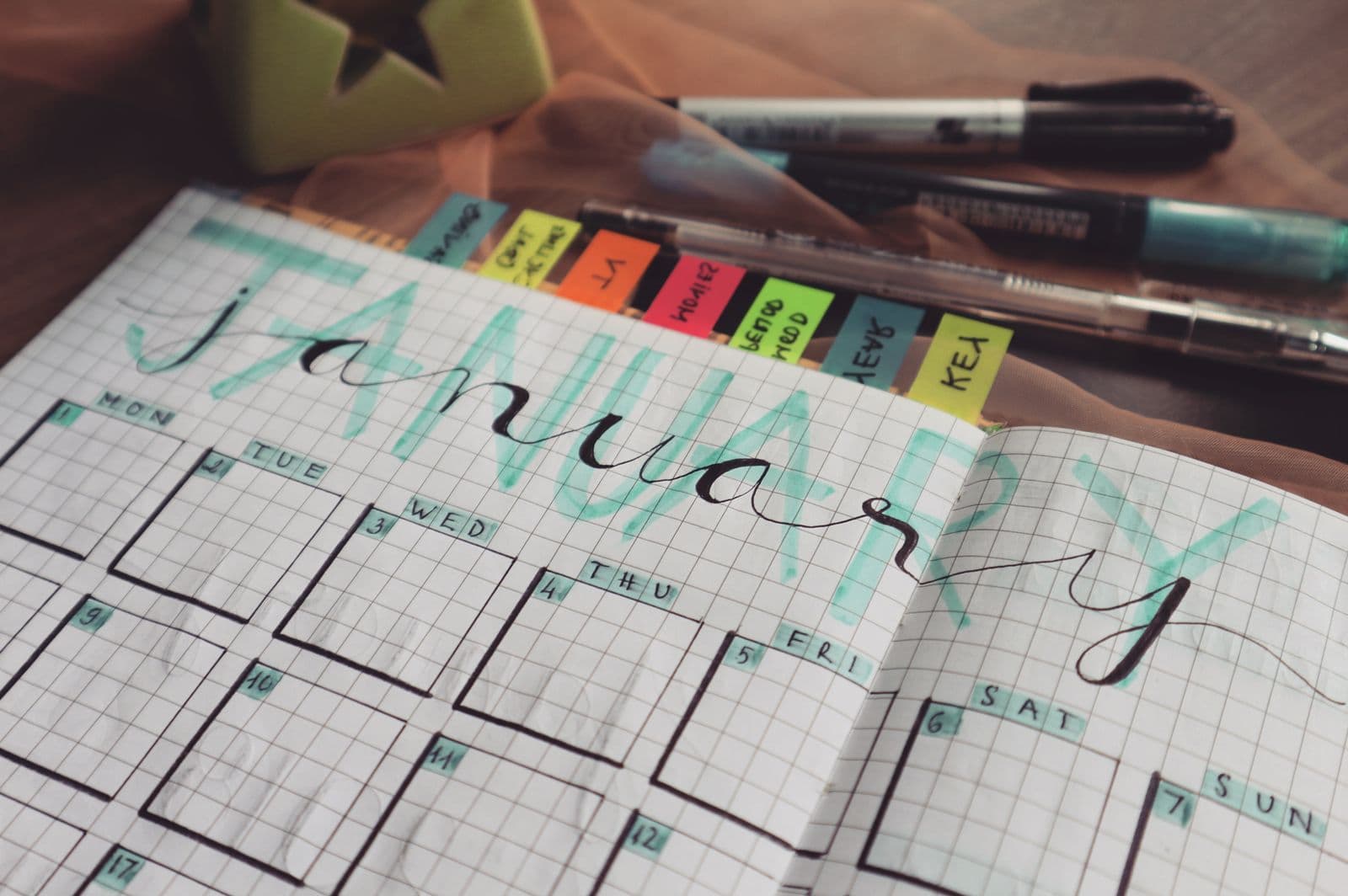 Handwritten January planner page with colorful tabs and pens on a desk