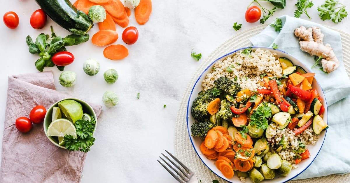 Overhead view of a colorful quinoa salad with fresh vegetables, greens, and herbs in a white bowl