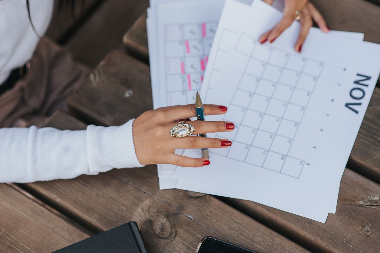 A woman's hand holding a pen over a November calendar page on a wooden table